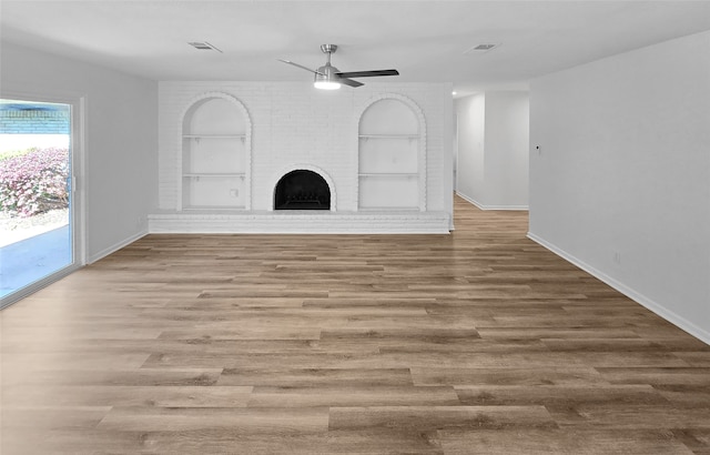 unfurnished living room with built in shelves, ceiling fan, hardwood / wood-style flooring, and a fireplace