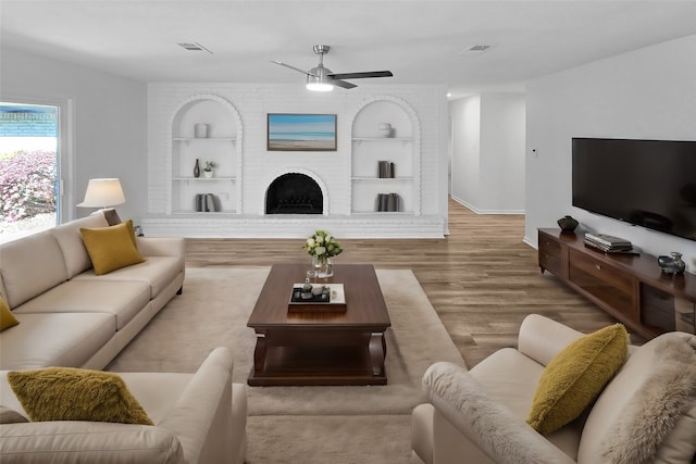 living room featuring built in features, ceiling fan, hardwood / wood-style flooring, and a fireplace