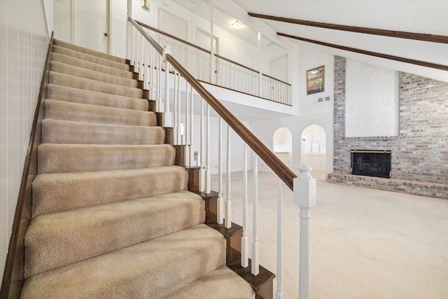 stairway with high vaulted ceiling, beam ceiling, carpet floors, and a fireplace