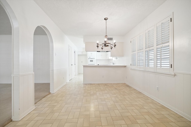 unfurnished dining area featuring light carpet, a chandelier, and a textured ceiling