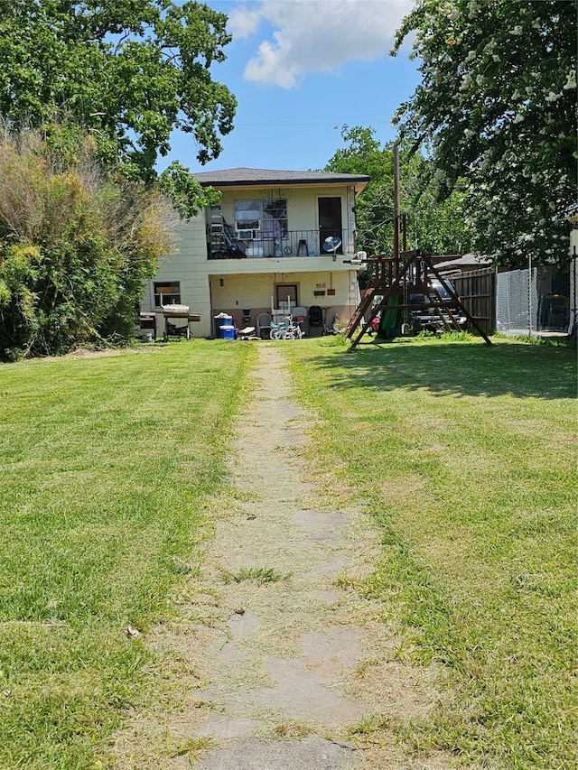 view of front of property featuring a front yard, a playground, and a balcony