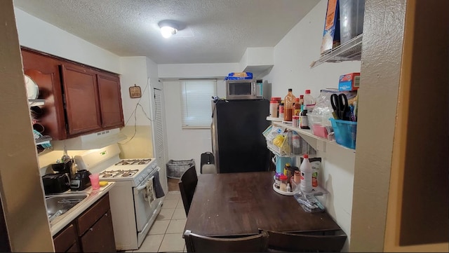 kitchen with fridge, white range with gas stovetop, a textured ceiling, and light tile flooring