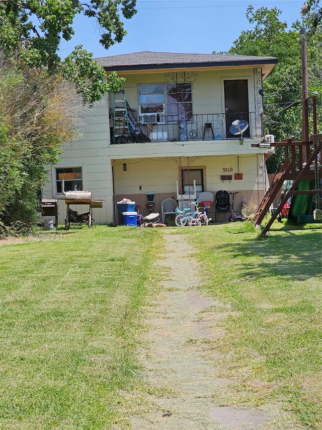 rear view of house featuring a balcony and a lawn