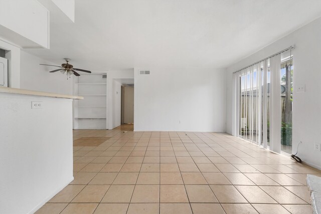 tiled spare room with ceiling fan and built in shelves