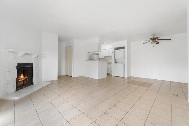 unfurnished living room with light tile floors, a premium fireplace, stacked washer and dryer, and ceiling fan