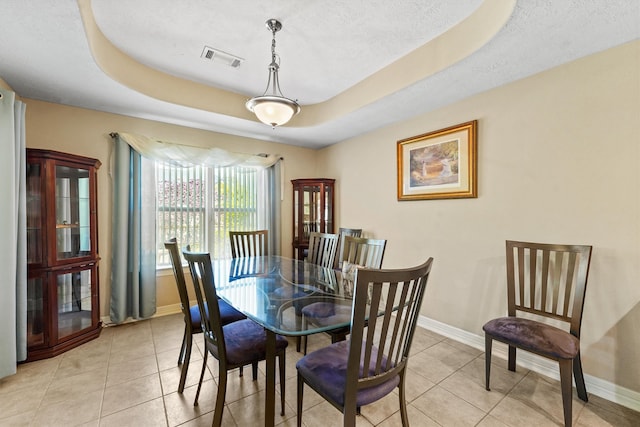 dining space featuring a textured ceiling, light tile flooring, and a raised ceiling