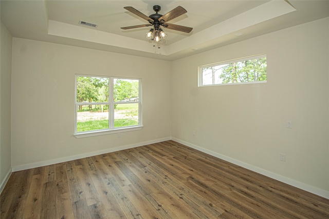 empty room featuring ceiling fan, dark wood-type flooring, a tray ceiling, and plenty of natural light