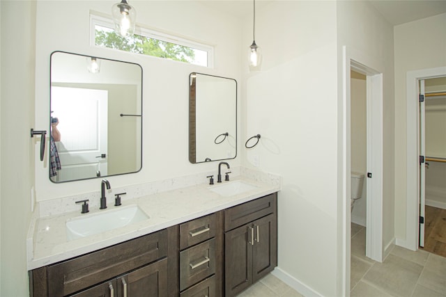 bathroom featuring toilet, vanity with extensive cabinet space, dual sinks, and tile flooring