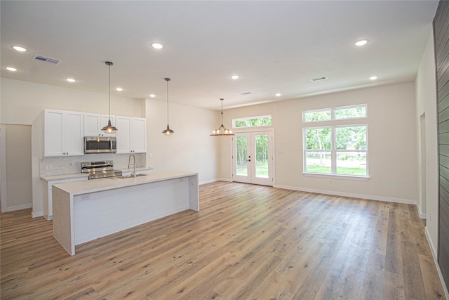 kitchen with hanging light fixtures, a kitchen island with sink, light hardwood / wood-style floors, stainless steel appliances, and white cabinets