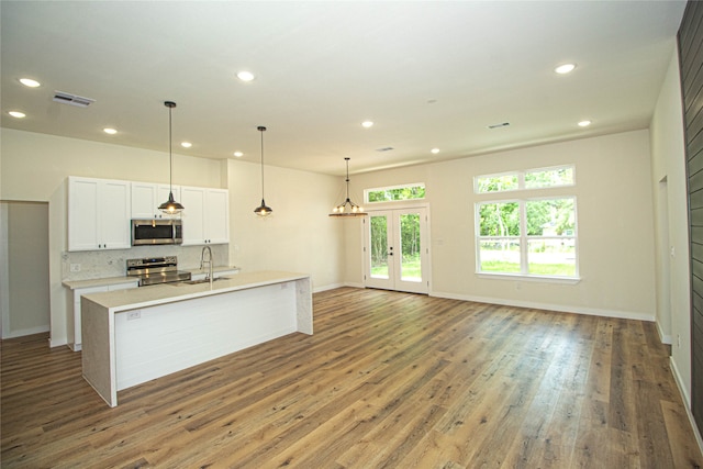 kitchen featuring dark hardwood / wood-style flooring, white cabinetry, an island with sink, stainless steel appliances, and pendant lighting