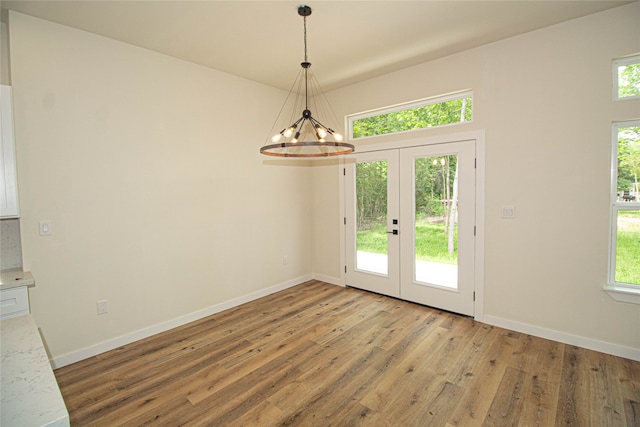 unfurnished dining area with a chandelier, light hardwood / wood-style floors, and french doors