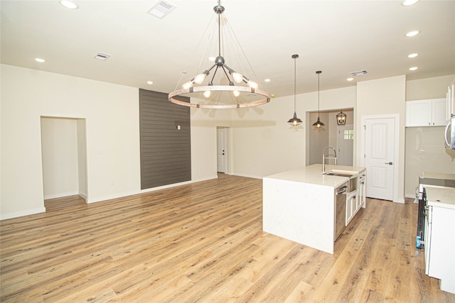 kitchen with an island with sink, light wood-type flooring, white cabinets, a chandelier, and pendant lighting