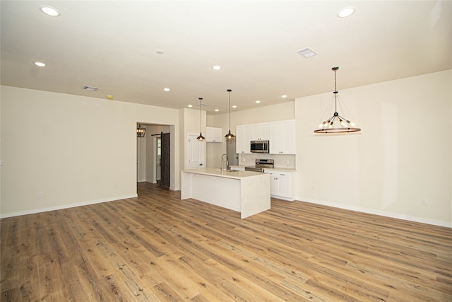 kitchen with light hardwood / wood-style floors, an island with sink, stainless steel appliances, white cabinets, and pendant lighting