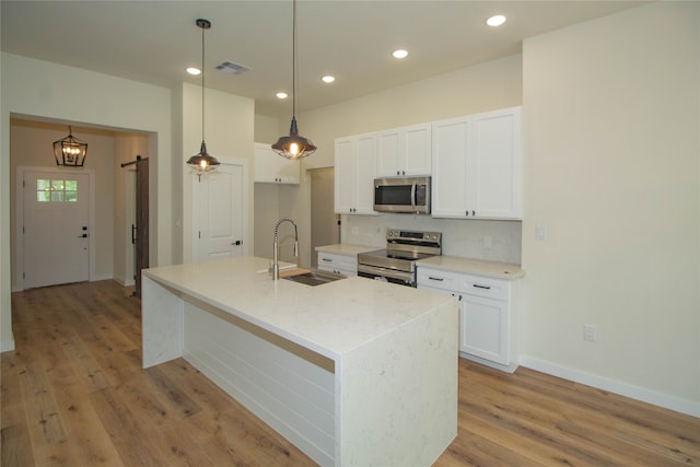 kitchen featuring an island with sink, pendant lighting, sink, light hardwood / wood-style flooring, and stainless steel appliances