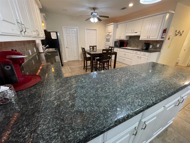 kitchen featuring backsplash, white cabinets, light tile floors, white oven, and ceiling fan