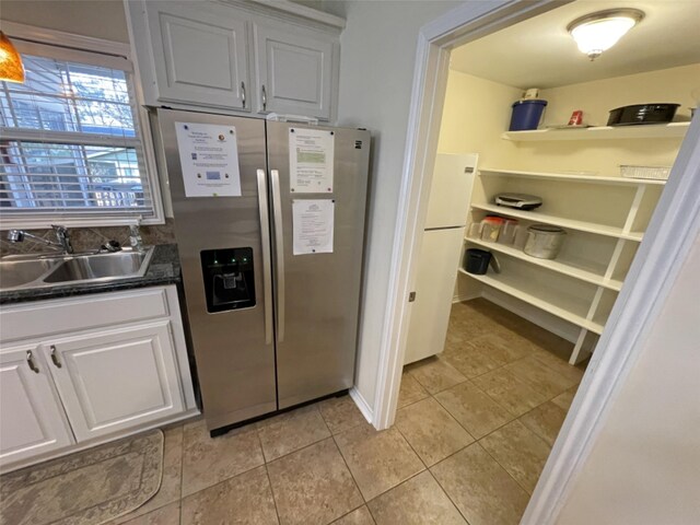 kitchen featuring stainless steel fridge, light tile floors, white cabinetry, and sink