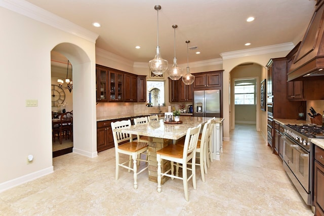 kitchen featuring stainless steel appliances, custom range hood, tasteful backsplash, light stone counters, and a center island