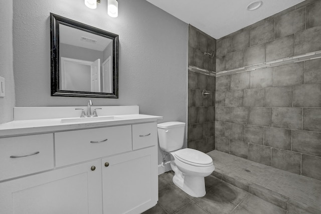 bathroom with tiled shower, tile flooring, toilet, and large vanity