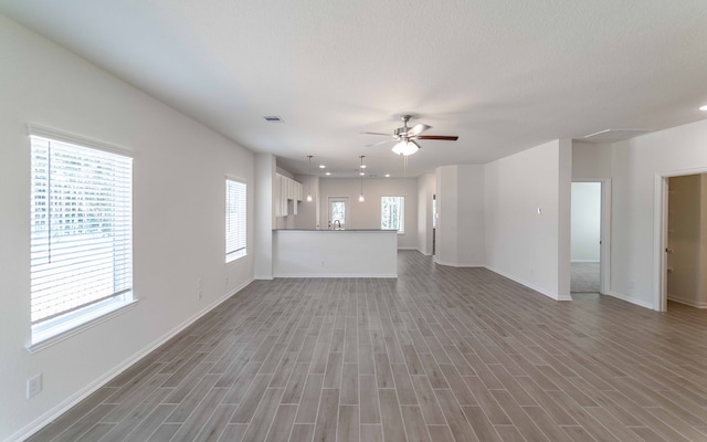 unfurnished living room with wood-type flooring, plenty of natural light, and ceiling fan