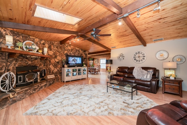 living room with wood ceiling, vaulted ceiling with skylight, a stone fireplace, and light hardwood / wood-style floors