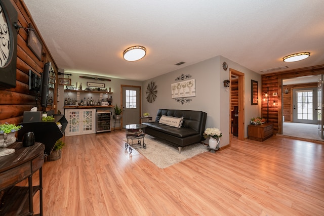 living room featuring rustic walls, indoor bar, light hardwood / wood-style flooring, wine cooler, and a textured ceiling