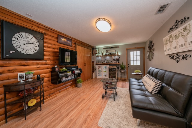 living room with light wood-type flooring, log walls, bar area, and a textured ceiling