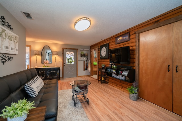 living room with light hardwood / wood-style floors, a textured ceiling, and wood walls