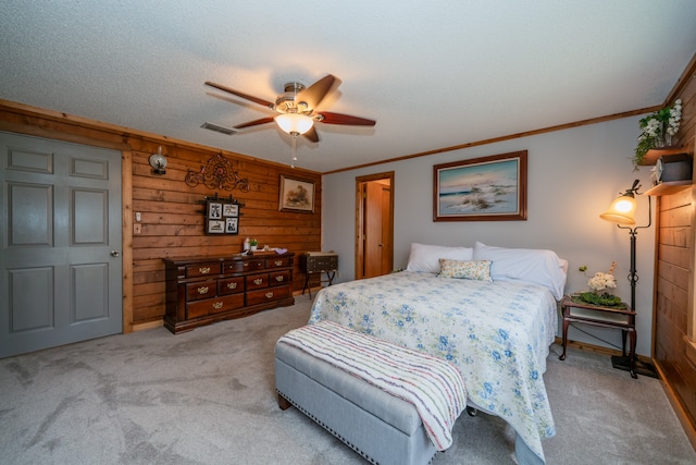 bedroom with light colored carpet, wood walls, ceiling fan, a textured ceiling, and ornamental molding