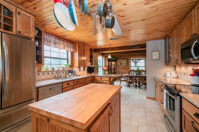 kitchen with appliances with stainless steel finishes, sink, butcher block counters, tasteful backsplash, and pendant lighting