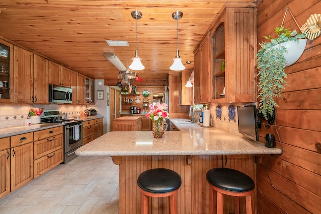 kitchen featuring kitchen peninsula, pendant lighting, a kitchen breakfast bar, backsplash, and stainless steel appliances