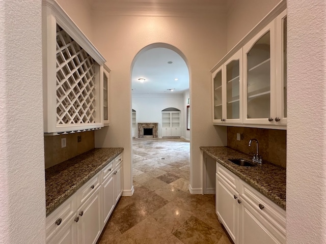 kitchen with backsplash, white cabinetry, dark stone countertops, and sink