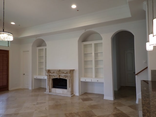 unfurnished living room featuring light tile floors, built in shelves, a chandelier, a fireplace, and a tray ceiling