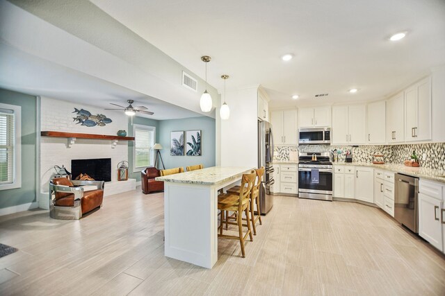 kitchen with pendant lighting, stainless steel appliances, a fireplace, ceiling fan, and white cabinets