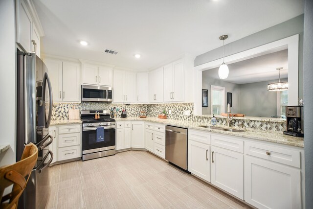 kitchen with hanging light fixtures, white cabinetry, backsplash, appliances with stainless steel finishes, and light stone counters