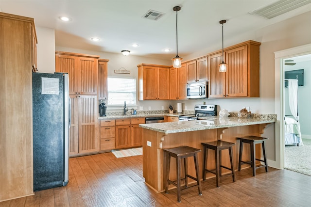 kitchen featuring kitchen peninsula, appliances with stainless steel finishes, decorative light fixtures, sink, and light wood-type flooring