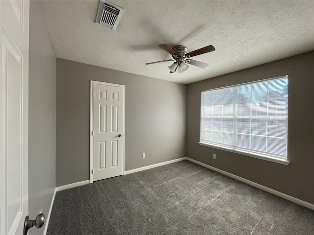 spare room featuring a textured ceiling, ceiling fan, and dark carpet