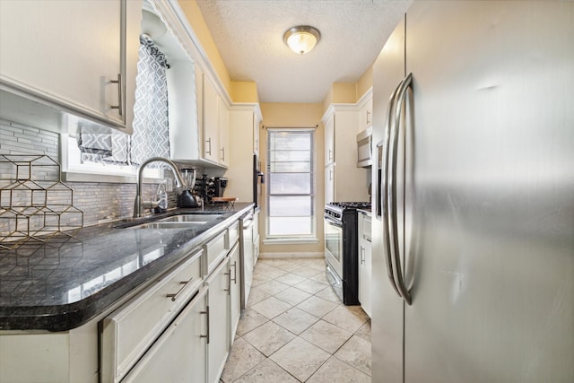 kitchen with appliances with stainless steel finishes, white cabinetry, backsplash, sink, and light tile flooring