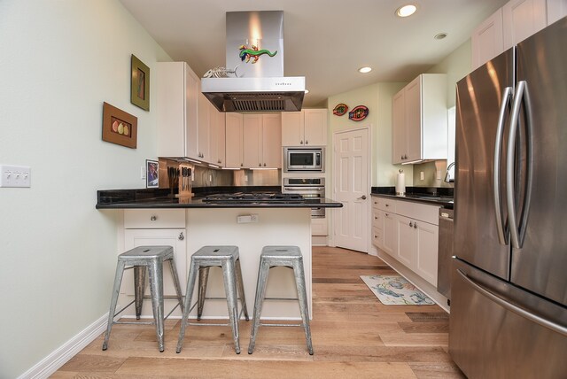 kitchen featuring a breakfast bar, white cabinets, range hood, light hardwood / wood-style floors, and stainless steel appliances