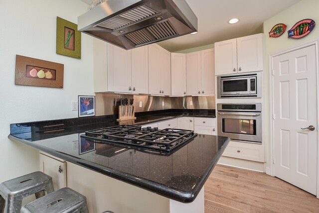 kitchen with appliances with stainless steel finishes, light hardwood / wood-style floors, range hood, and white cabinetry