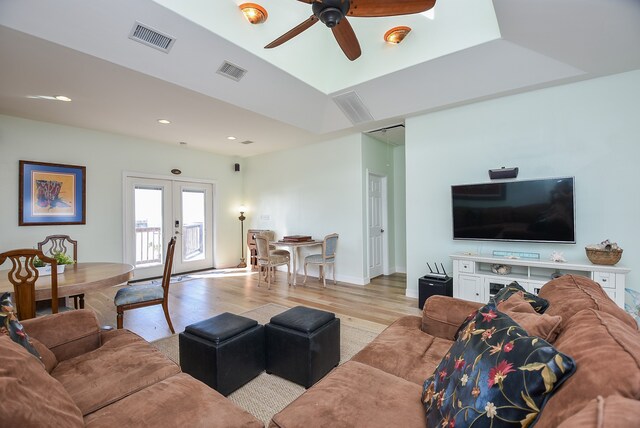 living room featuring french doors, ceiling fan, light wood-type flooring, and a tray ceiling