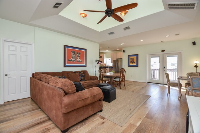 living room featuring french doors, light hardwood / wood-style flooring, ceiling fan, and a raised ceiling