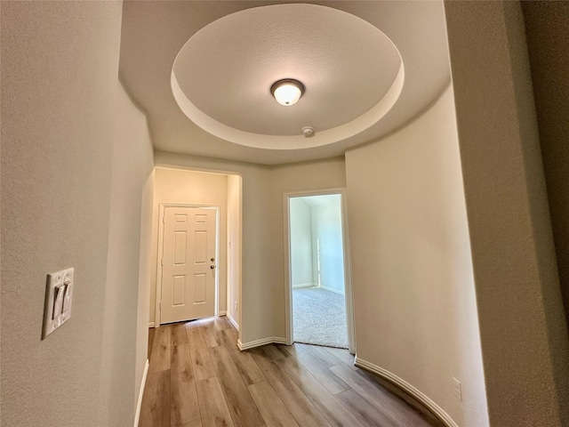 hallway with light wood-type flooring and a tray ceiling