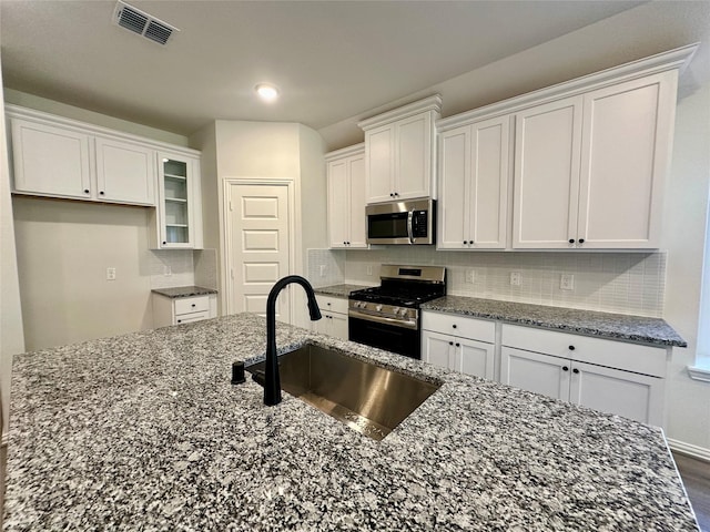 kitchen featuring stainless steel appliances, white cabinetry, dark stone counters, and sink