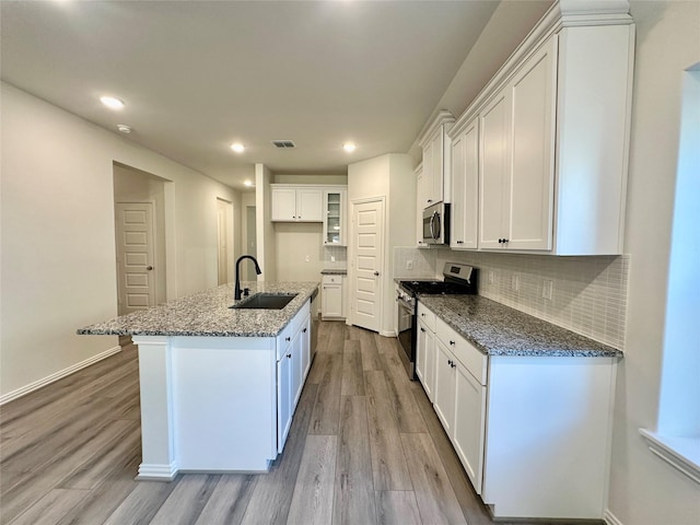 kitchen featuring dark stone counters, sink, an island with sink, appliances with stainless steel finishes, and white cabinetry