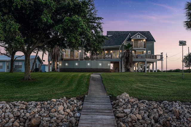 back house at dusk featuring a balcony and a yard