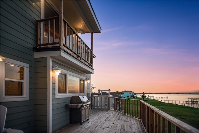 deck at dusk featuring a water view, a lawn, and area for grilling