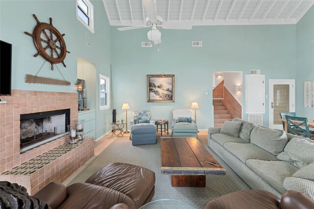 living room with ceiling fan, light hardwood / wood-style floors, wooden ceiling, a tile fireplace, and a high ceiling