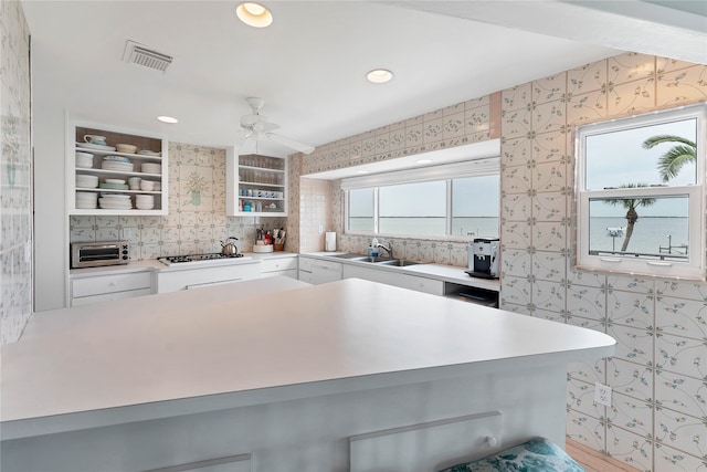 kitchen with sink, stainless steel gas stovetop, ceiling fan, white cabinetry, and tasteful backsplash