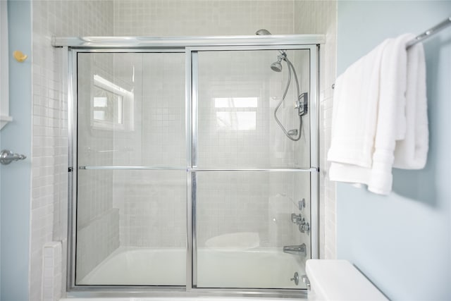 bathroom with toilet and bath / shower combo with glass door