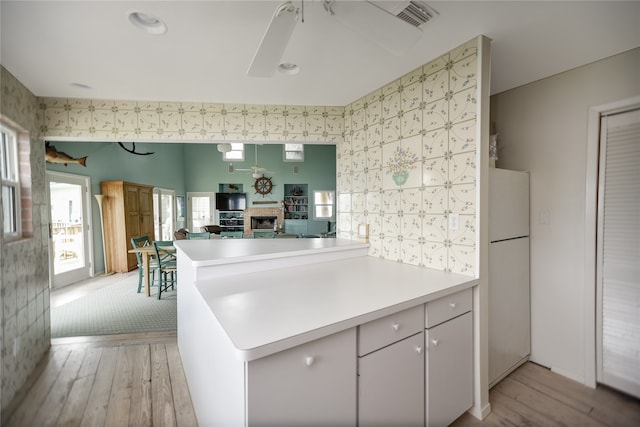 kitchen featuring white fridge, ceiling fan, light hardwood / wood-style floors, kitchen peninsula, and white cabinetry